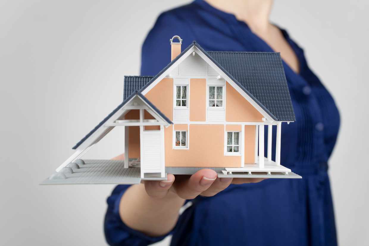  A lady holding a house structure, symbolizing home ownership or real estate concept.